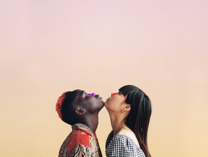 Two women touching chins wearing colorful Nözscreen in purple and red on their noses looking up.